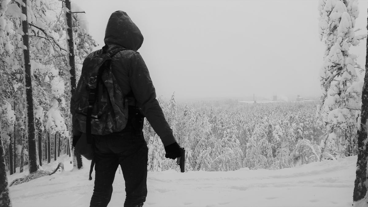 person carrying backpack standing on snow while holding pistol