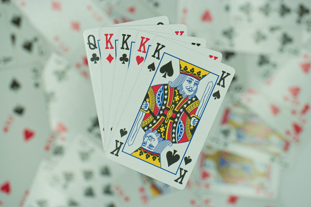 a hand holding four playing cards in front of a background of playing cards