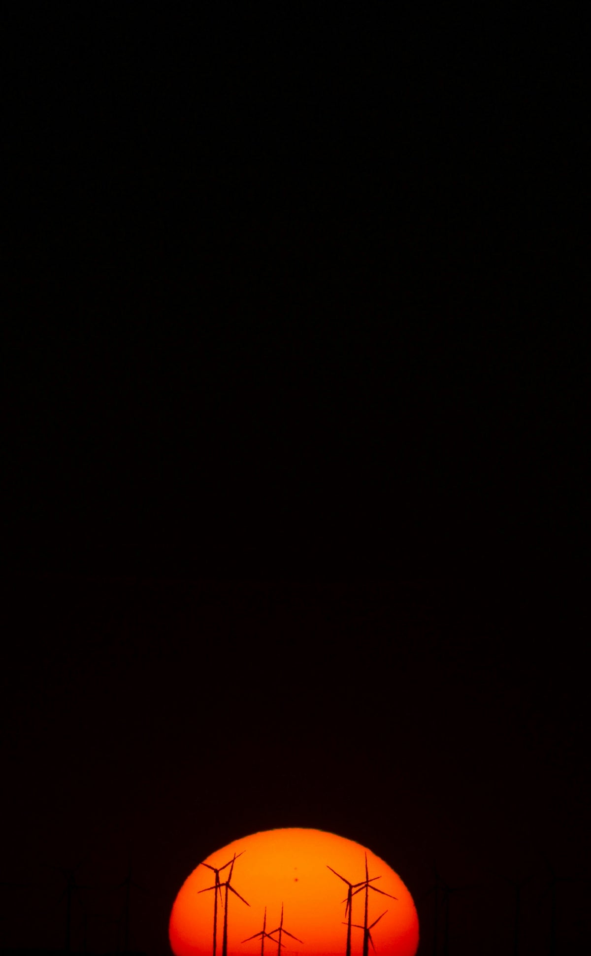 Wind turbines stand silhouetted against a setting sun.