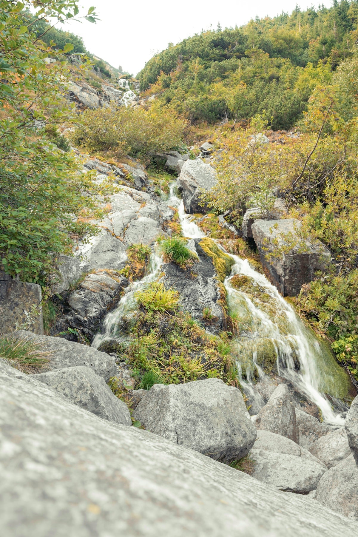 A rocky waterfall cascades down a hillside in autumn.