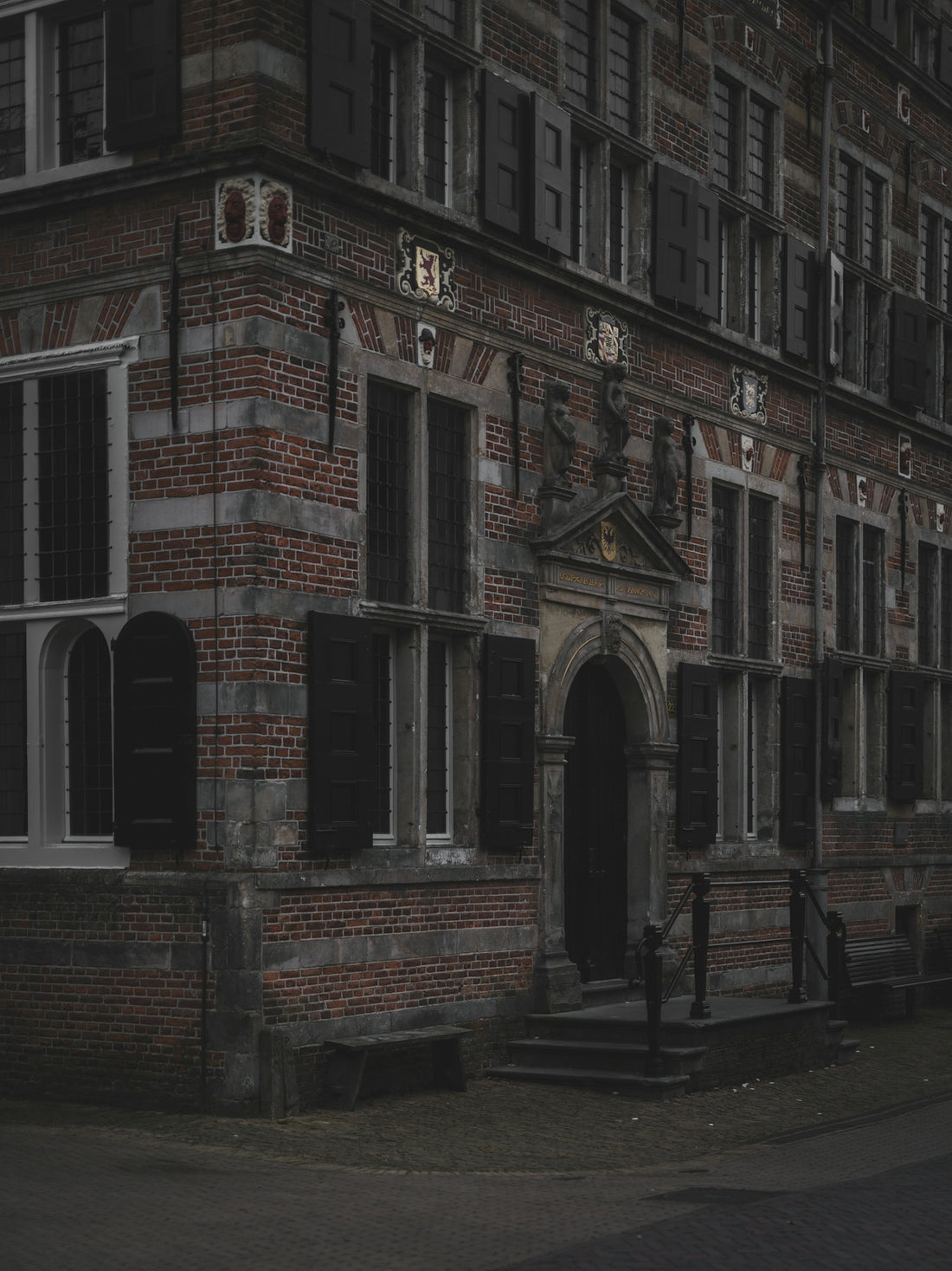 Old brick building with dark shutters and arched doorway.