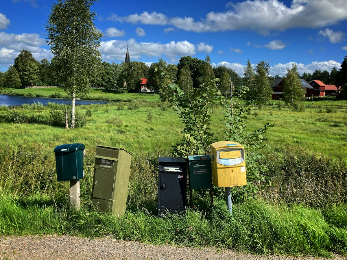 Mailboxes stand in a grassy field with a village background